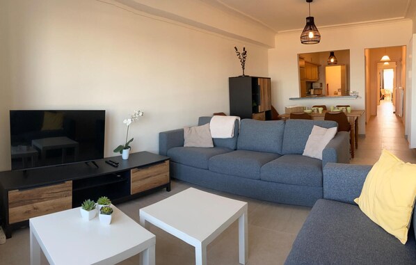 Un salón moderno con un sofá gris, un televisor de pantalla plana, una mesa de centro y una planta pequeña.
