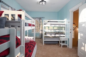 A bunk bed room with a desk and chair, carpeted floor, and a door leading to another room.
