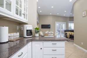 A modern kitchen with white cabinets, a coffee maker, and a dining area with a table and chairs.