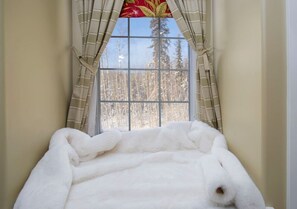 A window with a view of trees, curtains, and a white fluffy object.