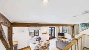 A spacious loft-style room with a dining area, a living area with a sofa and TV, and a staircase. - The Cote, Little Upton Farm (Ashey)
