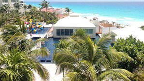 A resort with a swimming pool, palm trees, and a view of the ocean. - Renovated Studio in Cancun Beach (Cancún)