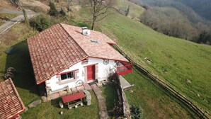 A white house with a red roof and a small porch, surrounded by a green hillside and a wooden fence. - 2 bedroom nice home in Bidarray (Bidarray)