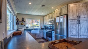 A modern kitchen with wooden cabinets, stainless steel appliances, and a large window providing natural light. - Saddleback - Rock Pond Condo 24 - right above base lodge (Rangeley)