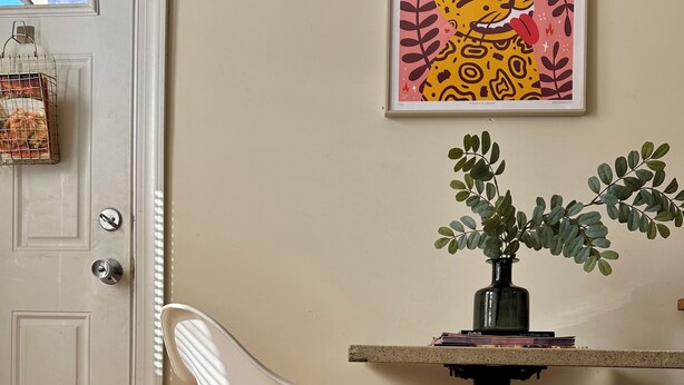Een kamer met een witte stoel, een tafeltje met een plant en een lijst met kunst aan de muur.
