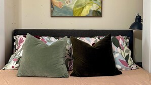 Een bed met kussens met een bloemenprint, een gebreide deken en een schilderij aan de muur.