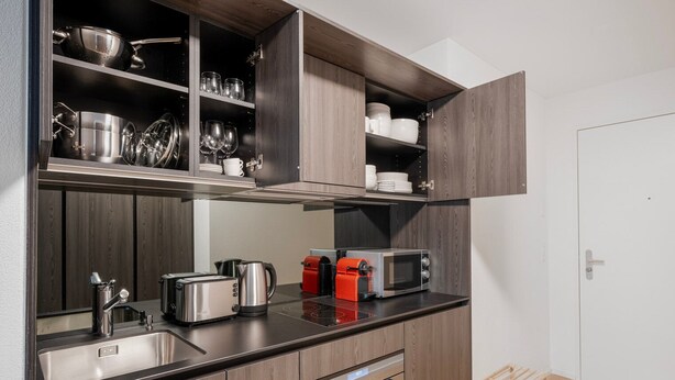 A compact kitchenette with a built-in oven, microwave, toaster, and kettle.