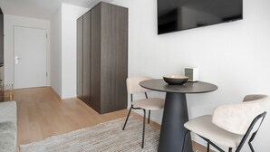 A modern living room with a round table, two chairs, a flat-screen TV mounted on the wall, and a wardrobe with a dark wood finish.