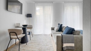 A modern living room with a sofa, chairs, a coffee table, and a TV on the wall.