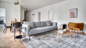 Een moderne woonkamer met een grijze bank, zwarte stoelen, een houten salontafel en een vloerkleed met een patroon.