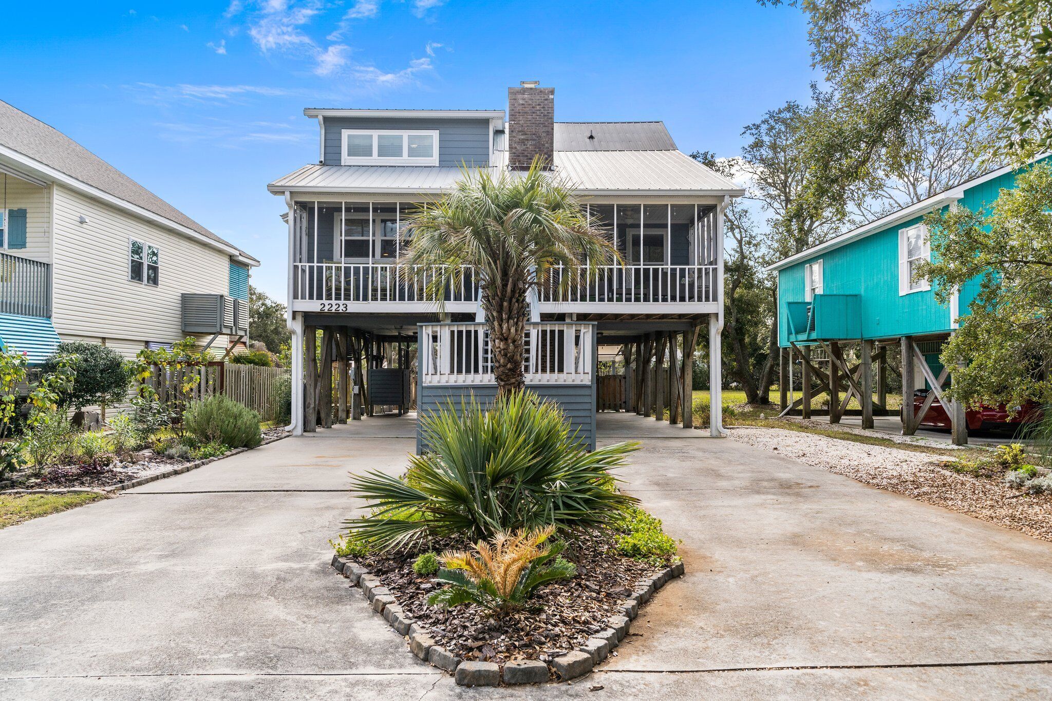 A two-story house with a balcony, a small garden with a palm tree, and a clear sky.