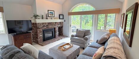 A living room with a fireplace, a television, and a large window.