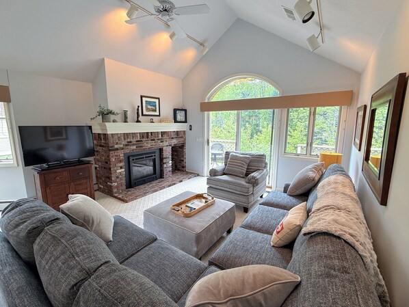 Una sala de estar con chimenea, televisor y un ventanal amplio.
