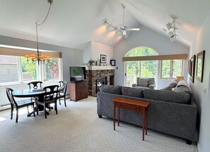 Een woonkamer met een open haard, een bank, een eettafel met stoelen, een televisie en een plafondventilator.