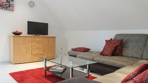 Un salon moderne avec un canapé, une table basse en verre, un meuble en bois et un téléviseur à écran plat.