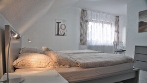 Une chambre à coucher avec un lit, des lampes de chevet, une chaise, un radiateur et une fenêtre avec des rideaux.