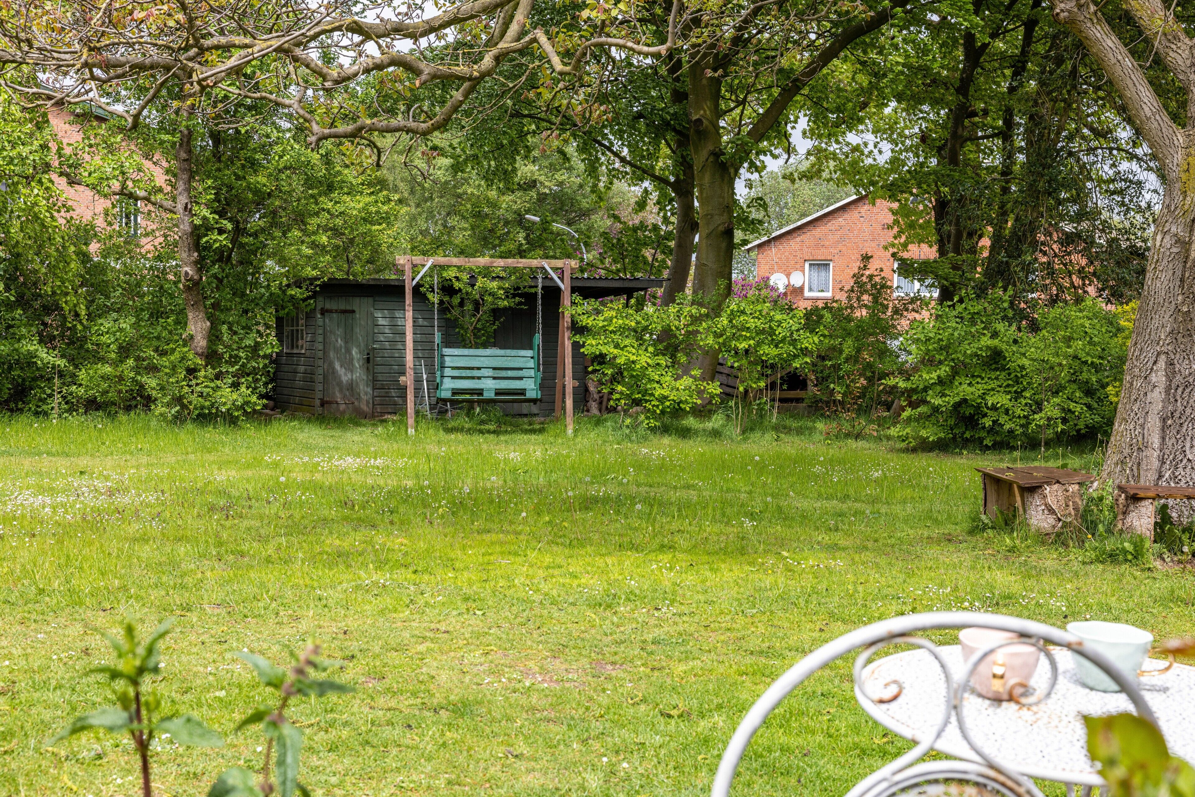 A grassy yard with a wooden swing set, a metal table with cups, and a brick building in the background.
