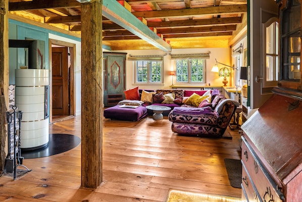 A wooden-floored living room with a sofa, ottoman, and a vintage refrigerator.