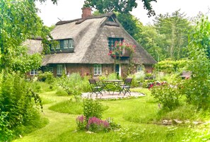 A thatched-roof house with a garden, a table with chairs, and a small patio area.