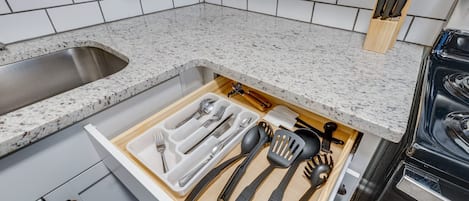 Una cocina con encimera de granito, pileta de acero inoxidable y organizador de cajones con utensilios.