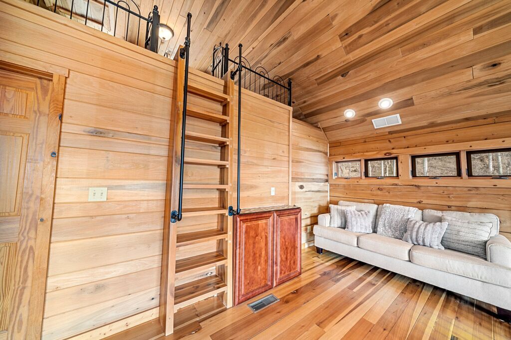 A wooden interior with a loft bed, a sofa, and a ladder.