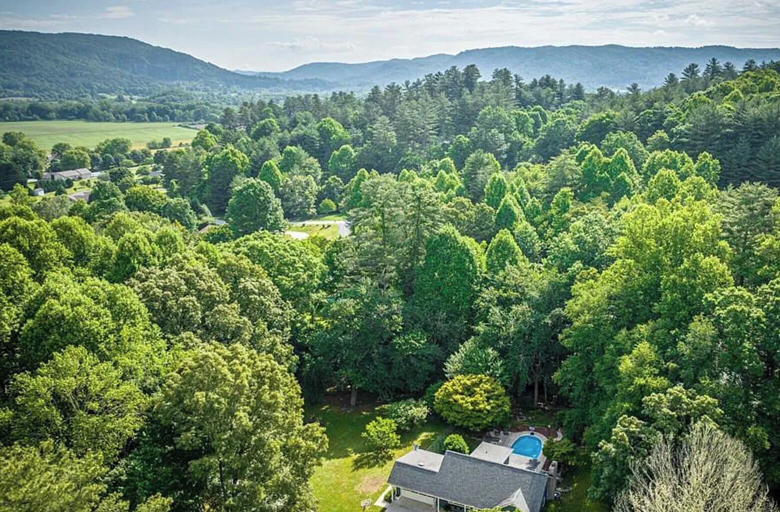 A house surrounded by dense forest with a visible swimming pool and a large lawn.