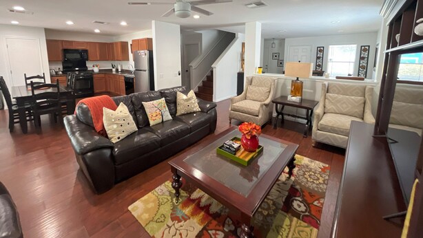 A modern living room with a black leather sofa, a coffee table, and two armchairs. A kitchen with wooden cabinets and a dining area with a table and chairs are visible in the background. - Top Location! Spacious Home Near Downtown & Events (Austin)