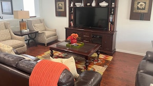 A living room with a leather sofa, a coffee table with a vase, a television, and a bookshelf. - Top Location! Spacious Home Near Downtown & Events (Austin)