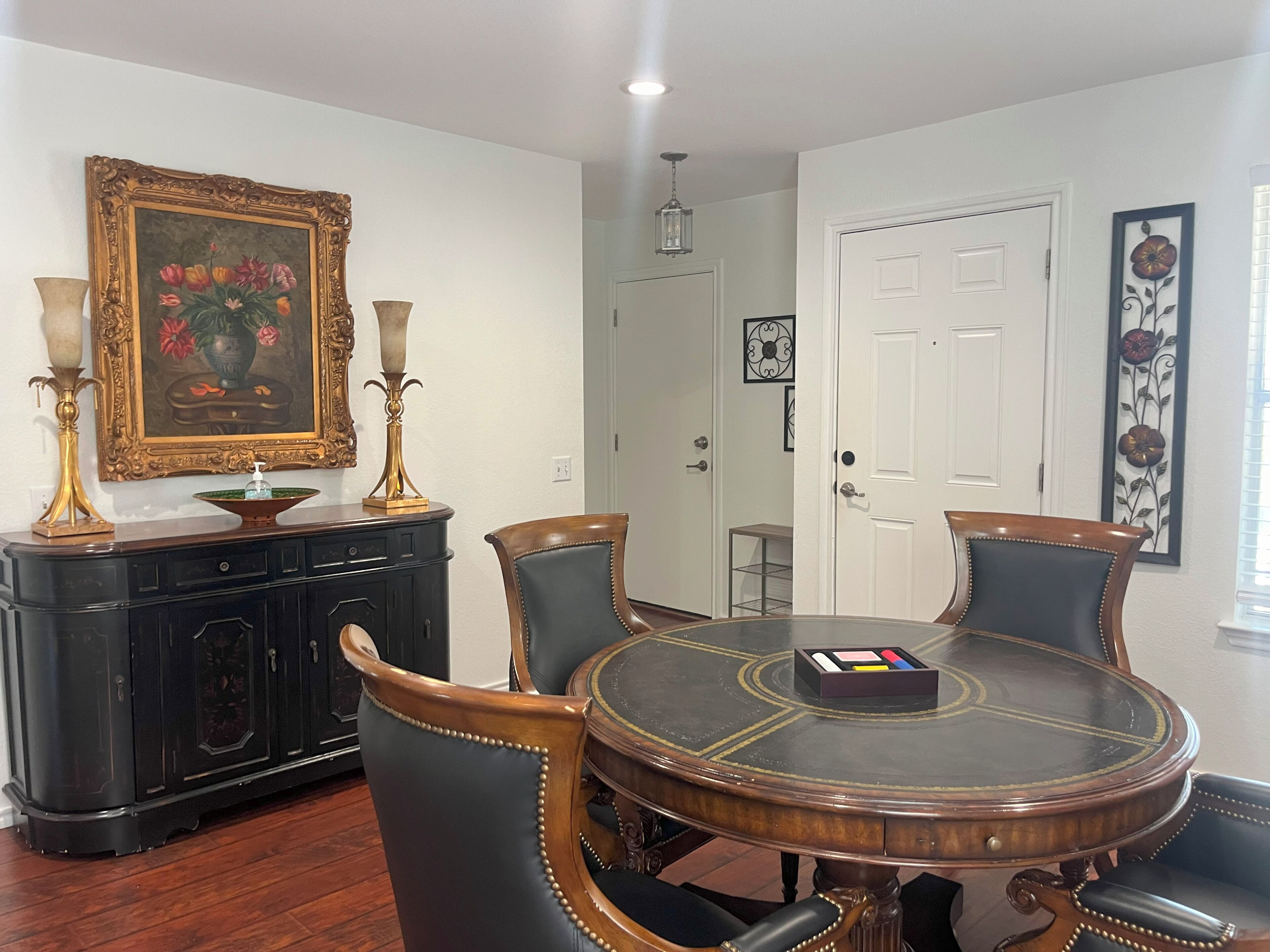 A dining room with a round table, black upholstered chairs, a black cabinet, and a framed painting of flowers.