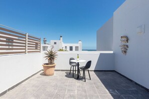 A rooftop terrace with a white wall, a potted plant, two chairs, a small table, and a bottle. - Big Bay Sea-view Apt Balcony & inverter (Cape Town)