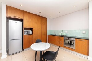 A compact kitchen with wooden cabinets, a stainless steel refrigerator, a microwave, an oven, and a small dining table with two chairs.