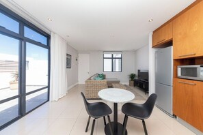 A modern kitchen with a dining area, a sofa, and a TV.
