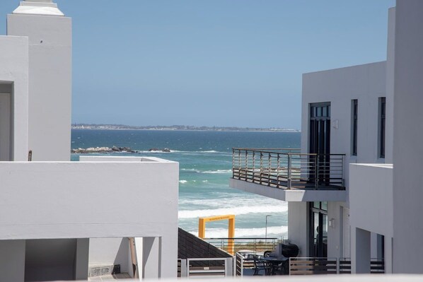 A modern building with a balcony overlooking the sea, featuring a clear view of the coastline and waves.