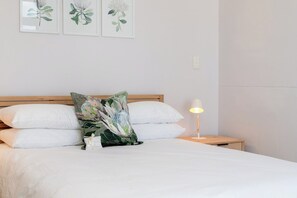 A neatly made bed with white linens, a single green floral pillow, and a bedside lamp on a wooden nightstand.