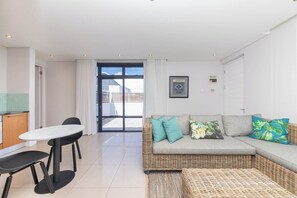 Sala de estar moderna com sofá, mesa de jantar e cadeiras. Uma janela grande oferece vista para o exterior.