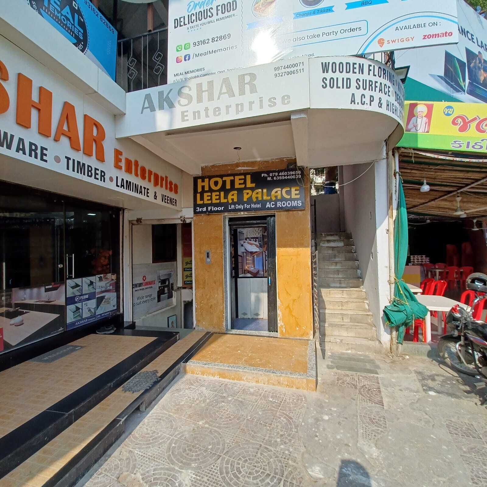 A hotel entrance with a sign for Hotel Leela Palace, a sign for Akshar Enterprise, and various other signs for businesses like Swiggy and zomato.