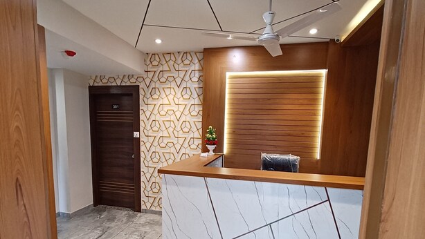 Una zona de recepción con mostrador de mármol, paneles de madera, ventilador de techo y pared con diseño.