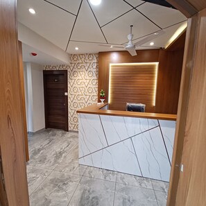 Un espace d’accueil doté d’un comptoir en marbre, de lambris en bois, d’un ventilateur de plafond et d’un mur orné de motifs.