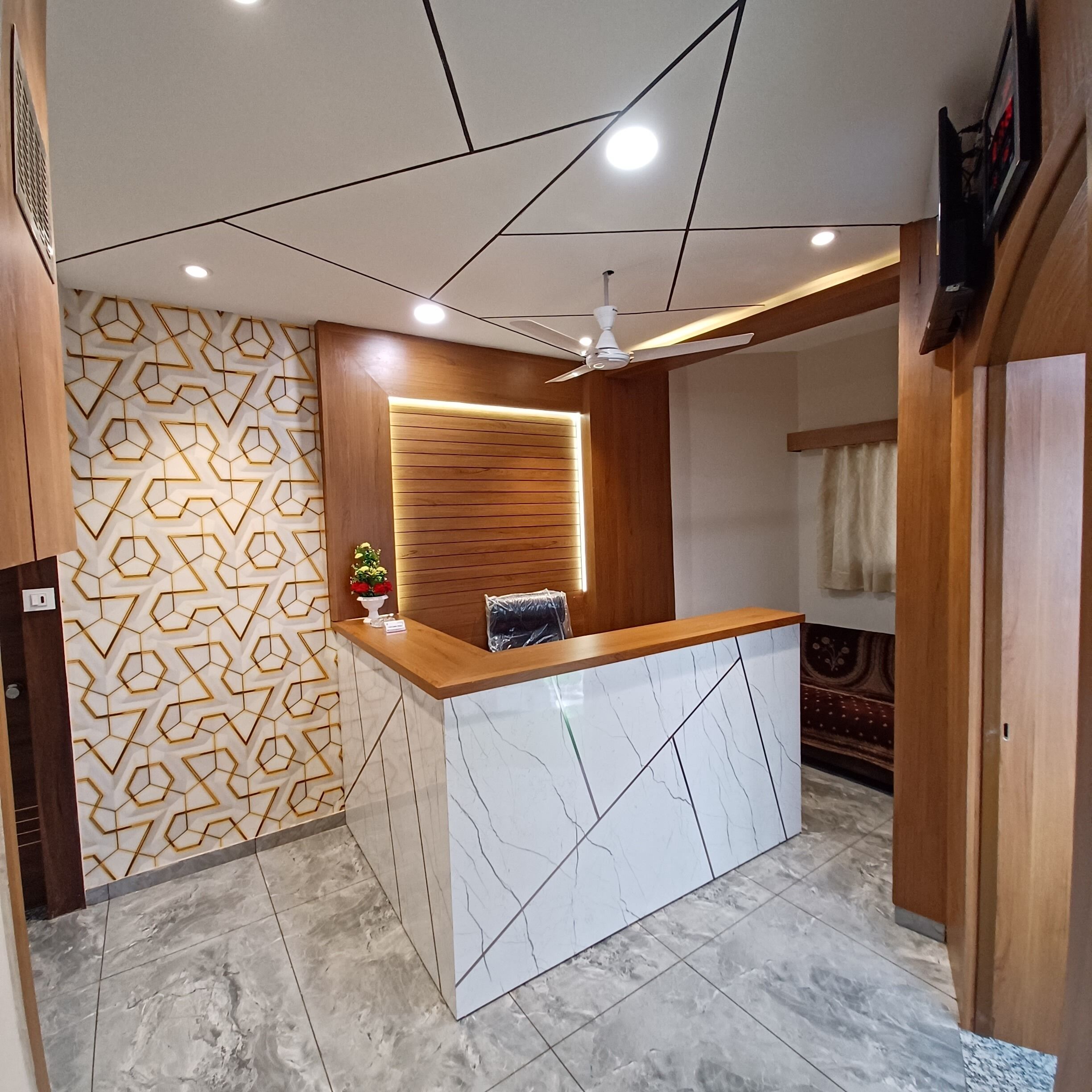 A reception area with a wooden reception desk, a geometric patterned wall, and a ceiling fan.