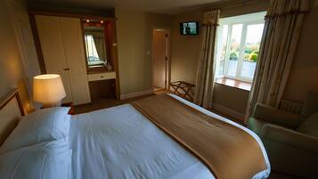 A hotel room with a large bed, a chair, a TV, and a window with curtains.