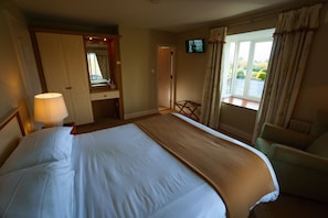 A hotel room with a large bed, a chair, a TV, and a window with curtains. - Park Lodge (Abbeyfeale)
