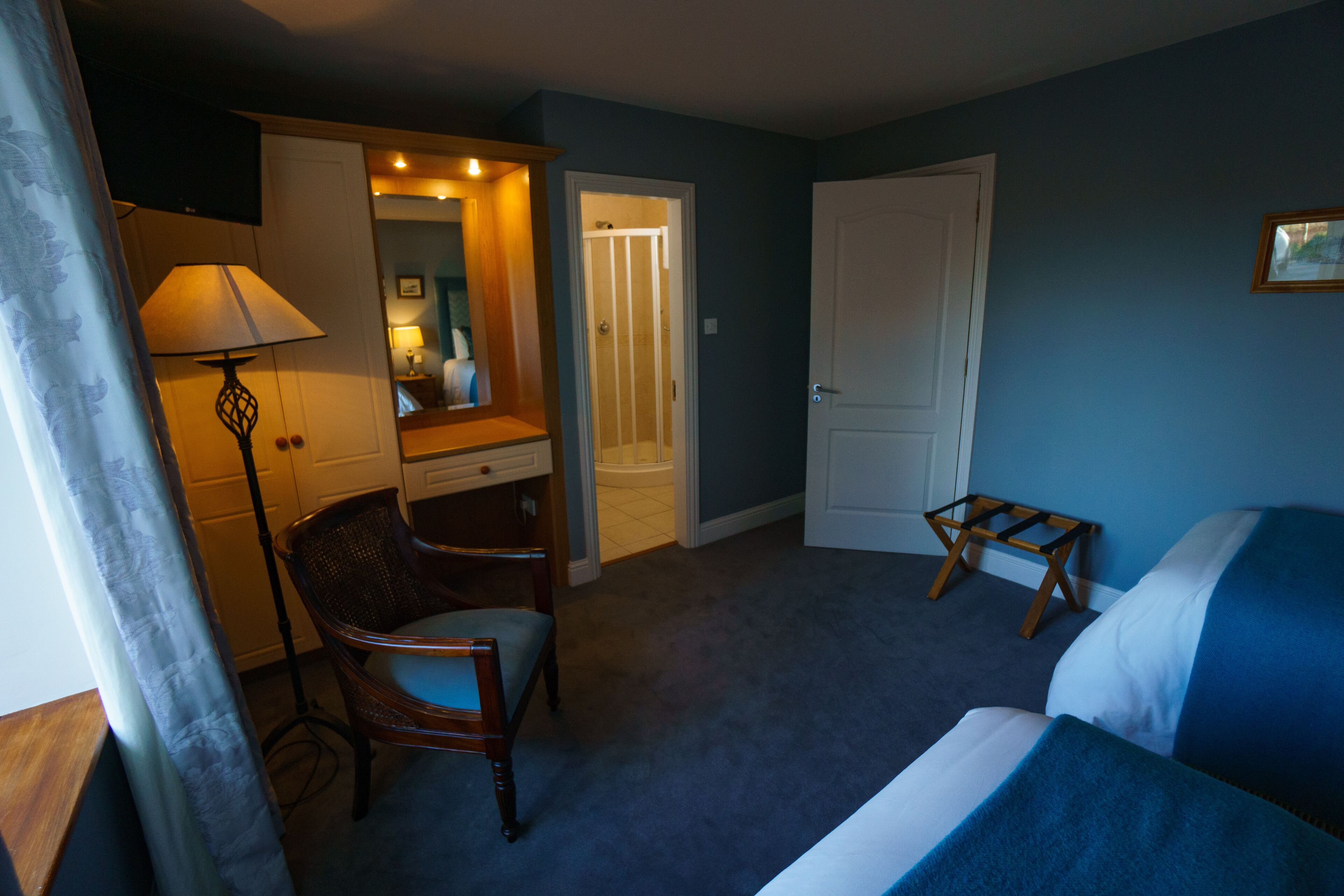 A hotel room with a bed, a chair, a desk, a lamp, and a door leading to another room.