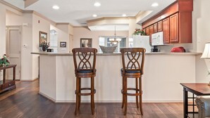 A kitchen with wooden cabinets, a white refrigerator, and two wooden bar stools. - Family Getaway • Show & Golf Discounts • Resort Amenities (Branson)