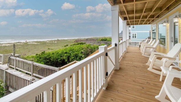 A wooden deck with white railings, white plastic chairs, and a view of the ocean. - Hobbs Realty - Oceanfront Home w/Expansive Decks and Second Living Area w/Futon (Holden Beach)