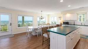 A kitchen with a large island, white cabinetry, and a view of the ocean. - Hobbs Realty - Oceanfront Home w/Expansive Decks and Second Living Area w/Futon (Holden Beach)