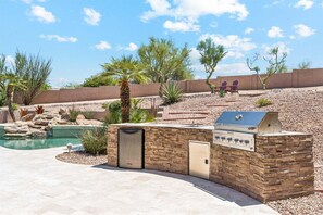 A backyard with a pool, a barbecue grill, and a stone wall. - Hillside Tranquility - Desert Views, Heated Pool, Outdoor Kitchen & Light-Filled Luxury (Fountain Hills)