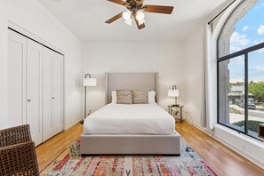 A bedroom with a large bed, two bedside lamps, a ceiling fan, a view of the outside, and a large window. - Hillside Tranquility - Desert Views, Heated Pool, Outdoor Kitchen & Light-Filled Luxury (Fountain Hills)