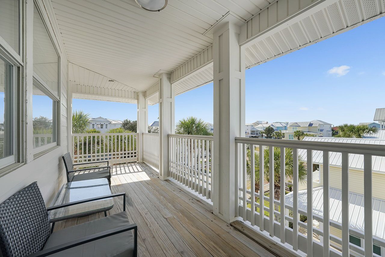 A covered outdoor balcony with white railings, a glass table, and chairs.