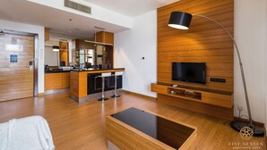 A modern living room with a wooden floor, a black TV on a wooden wall, a coffee machine, and a bar area. - Dua Sentral Kuala Lumpur, Roam (Kuala Lumpur)