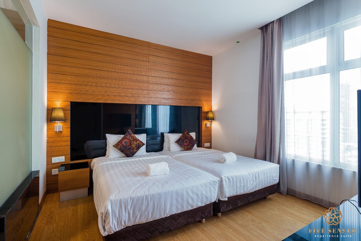 Ein Hotelzimmer mit zwei Betten, Holzvertäfelung an der Wand, einem großen Fenster mit Vorhängen und einem Nachttisch mit Lampe.